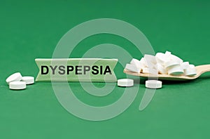 On a green surface, a wooden spoon with pills and a sign with the inscription - DYSPEPSIA