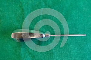 On  green surgical drape lies an awl for an operation