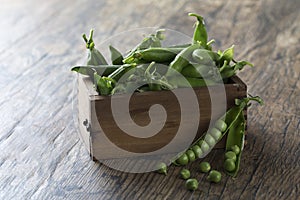 Green sweet peas in wooden box on brown wood surface