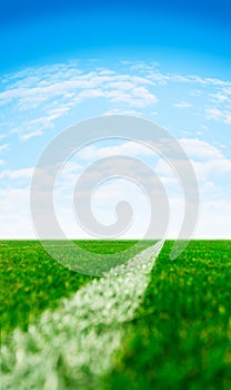Green synthetic grass sports field with a white line in perspective and blue sky