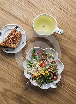 Green tea, crispy wholegrain toast and salad with canned tuna, boiled egg, arugula, cherry tomatoes and corn on a wooden
