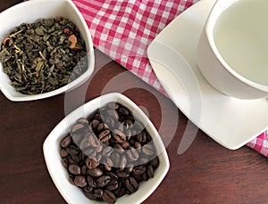 Green tea leaves and black coffee beans , white Cup with hot water on a pink tablecloth in the box on a brown background