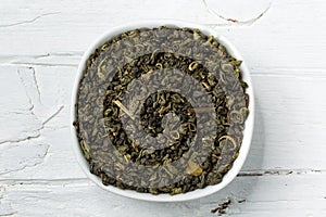 Green tea leaves gunpowder in white bowl on wooden background.