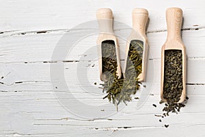 Green tea leaves in scoop on white wooden background.