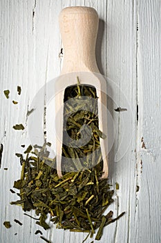 Green tea leaves with scoop on wooden background