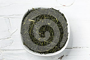 Green tea leaves sencha in white bowl on wooden background.