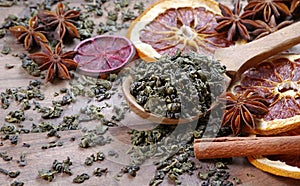 Green tea leaves in a wooden spoon, dried citruses, cinnamon and anise. tea and spices