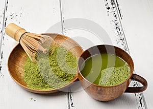 Green tea matcha powder in a wooden bowl with whisk and a green tea cup matcha