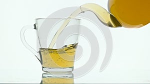 Green tea pouring into glass cup from teapot on white background