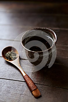 Green tea sencha in a traditional, japanese tea cup and sencha leaves on a wooden tea spoon.