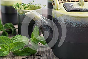 Green tea in teapot with small cups over with mint, wooden background