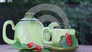 A green teapot and a green mug on a saucer with a sprig of red currant on the table