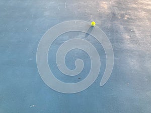 Green tennis ball is on a blue tennis court with bright sunshine