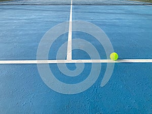 Green tennis ball is on the white line and the black net is in the middle of the court