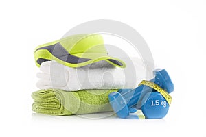 Green tennis headband cap on a pile of white and green towels with two blue vinyl coated dumbbells wrapped with yellow measuring t