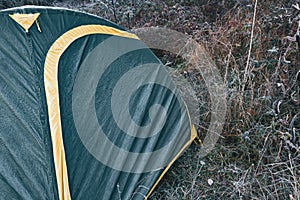 Green tent on dry grass in cold autumn forest. Fabric froze, covered with frost. Traveling in wild