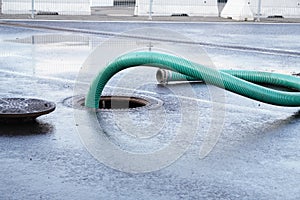 The green thick hose from a sewer pit, pumping sewage or sewage from collector in city. water drainage. Sewer manhole with an open