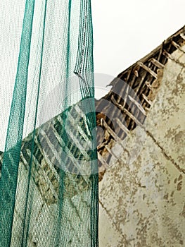 Green thin net hanging covering half of the view on weathered old broken building wall under construction with wooden