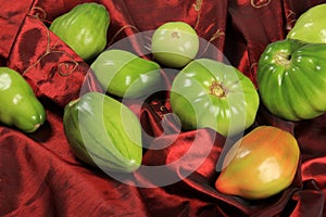 Green tomatoes ripen on a red fabric. group of green tomatoes on top of a fabric