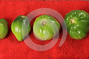 Green tomatoes ripen on a red fabric. group of green tomatoes on top of a fabric