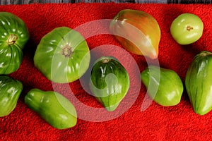 Green tomatoes ripen on a red fabric. group of green tomatoes on top of a fabric