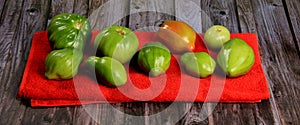 Green tomatoes ripen on a red fabric. group of green tomatoes on top of a fabric