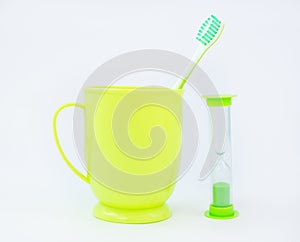 Green toothbrush in cup and hourglass