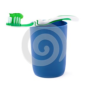 Green toothbrush with paste lying on blue plastic cup isolated over white background