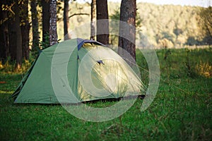 A green tourist tent stands in the forest, illuminated by rays of light.