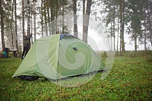 A green tourist tent stands in the forest, illuminated by rays of light.