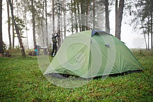 A green tourist tent stands in the forest, illuminated by rays of light.