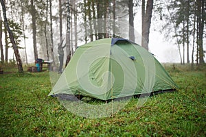 A green tourist tent stands in the forest, illuminated by rays of light.