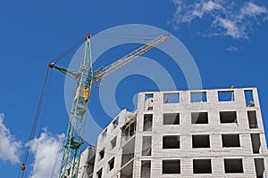 Green tower crane with yellow cabin and jib working on the construction site at the top floors of the building