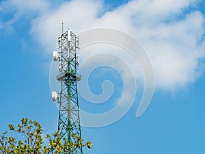 Green tower with microwave link and TV transmitter antennas, telecommunication mast antennas wireless technology over blue sky