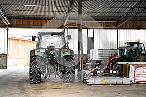 Green tractor with big wheels in garage near agricultural fixtures at daytime