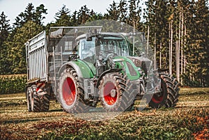 Green tractor with a loading wagon at a meadow