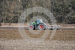 Green tractor plowing field at the forest