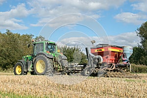 A green tractor with a seed drill in a stubble field