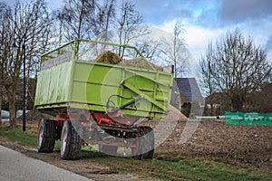 Green tractor trailer stands on the roadside next to a field