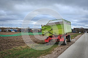 Green tractor trailer stands on the roadside next to a field