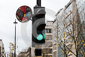 Green Traffic Light Signal and Traffic Convex Mirror with the Reflection of the red bus, London, England, UK