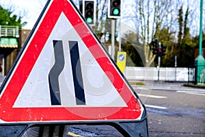 Green Traffic Lights Behind A Road Narrows Warning Triange With No Cars Or People