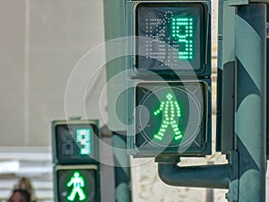 2 green traffic lights for pedestrians on the crosswalk counting down in 9 second.