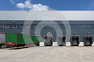 Green trailer in front of a loading door at a warehouse under a blue sky