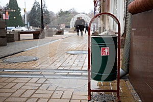 green trash bin with a red sticker near the entrance to the building on the background of a blurred park