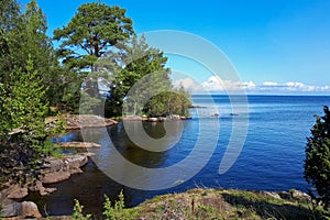 Green trees and grass on shore of the blue Lake Ladoga. Bay in the rocks on a clear summer sunny day. Blue sky with white