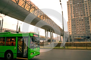 Green trolleybus rides on the road in city. against the backdrop of high-rise buildings and on top pedestrian