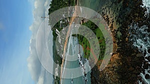 Green tropical rocky island in the middle of blue-green sea washed by waves aerial view vertical. Parrot Rock in Mirissa