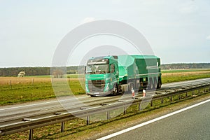 A green truck transports bulk cargo in a closed semi-trailer on a highway.