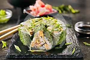 Green uramaki sushi roll with rice, cream cheese, fried salmon, tomatoes, beijing cabbage, green onion, dill and spicy sauce close